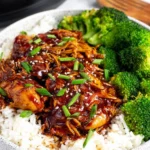 No-Fuss Slow Cooker Honey Garlic Chicken served over fluffy white rice with steamed broccoli, topped with sesame seeds and sliced green onions.