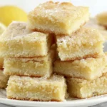 Plate of Lemon Sugar Cookie Bars stacked high with fresh lemon in the background
