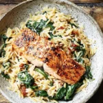 One Skillet Salmon with Lemon Orzo served in a bowl with golden-seared salmon, creamy lemon orzo pasta, and wilted spinach.