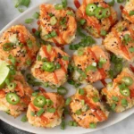 Spicy Salmon Crispy Rice bites with jalapeño slices, sesame seeds and sriracha drizzle served on a white platter