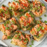 Spicy Salmon Crispy Rice squares topped with sriracha, sesame seeds and green onions on a white plate