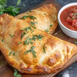 Air Fryer Calzones with crispy golden crust served with marinara sauce on a wooden board
