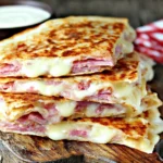 Corned Beef and Swiss Reuben Quesadillas stacked on a wooden board with melted Swiss cheese and a creamy dipping sauce