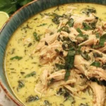 Crock Pot Thai Ginger Chicken Soup topped with shredded chicken and chopped herbs in a creamy ginger coconut broth with lime beside the bowl