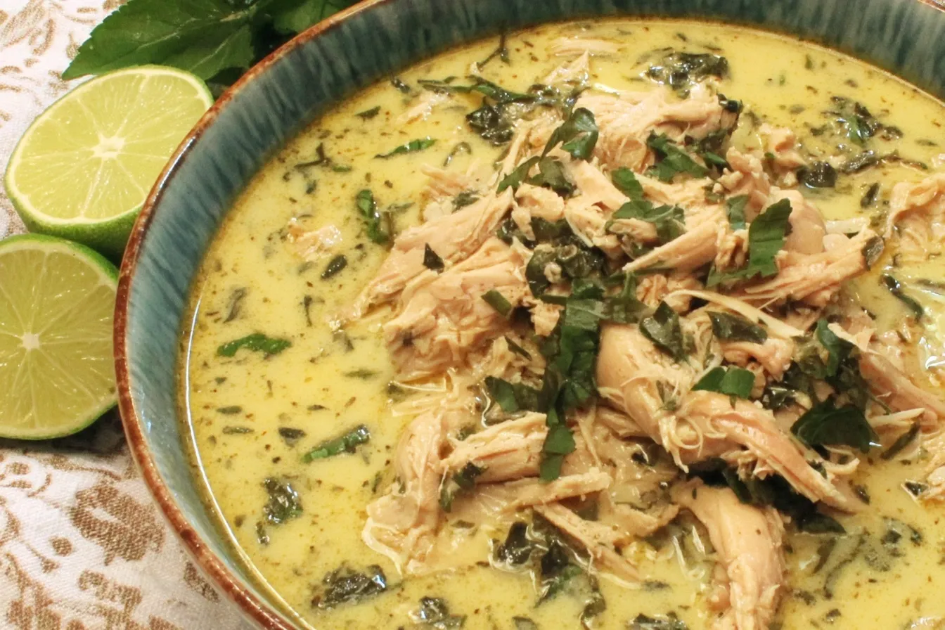 Crock Pot Thai Ginger Chicken Soup topped with shredded chicken and chopped herbs in a creamy ginger coconut broth with lime beside the bowl