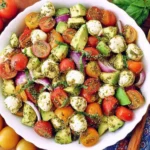 Overhead Avocado Salad Tomatoes Mozzarella Basil Pesto with red and yellow cherry tomatoes, avocado chunks, mozzarella pearls, cucumber, and red onion.