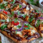 BBQ Chicken Flatbread on parchment with melty cheese, BBQ chicken, red onion, sliced jalapeños, and fresh cilantro, served with extra BBQ sauce.