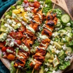 Chopped Buffalo Chicken Skewer Salad topped with grilled buffalo chicken skewers, cucumbers, tomatoes, avocado, blue cheese, and creamy herb dressing.