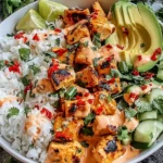 Coconut Chicken Rice Bowl with charred chicken cubes, fluffy jasmine rice, sliced avocado, cucumber, cilantro, chili flakes, and creamy coconut sauce.