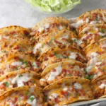 Baked Chicken Bacon Ranch Tacos baked crispy in a casserole dish with melted cheese, bacon crumbles, and ranch drizzle.