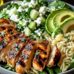 Grilled Chicken Orzo Salad bowl with char-grilled chicken slices, orzo, avocado, cucumber, feta, leafy greens, and fresh herbs.