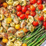 Pesto Chicken Tortellini and Veggies in a skillet with pesto-coated chicken, tortellini, asparagus, and cherry tomatoes.