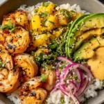 Shrimp and Avocado Bowl over fluffy white rice with charred chili shrimp, mango salsa, sliced avocado, pickled red onions, and creamy sriracha-lime sauce.