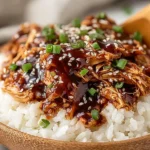 Sweet Crock Pot Teriyaki Chicken close-up on steamed white rice with thick teriyaki glaze, sesame seeds, and green onions in a wooden bowl.