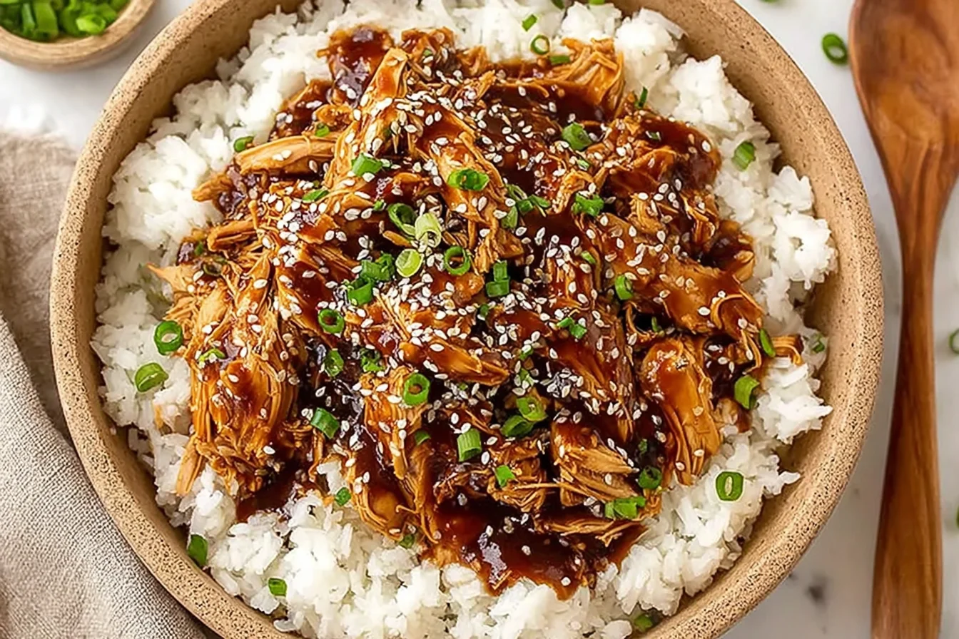 Sweet Crock Pot Teriyaki Chicken piled over fluffy white rice, topped with sesame seeds and sliced green onions in a rustic bowl.