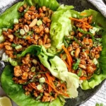 Thai Chicken Lettuce Wraps on a plate with butter lettuce cups filled with sweet chili ground chicken, shredded carrots, scallions, peanuts, and sesame seeds.