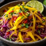 Vibrant Mango Slaw with shredded purple cabbage, sliced mango, red chili, cilantro, and fresh lime in a rustic bowl.
