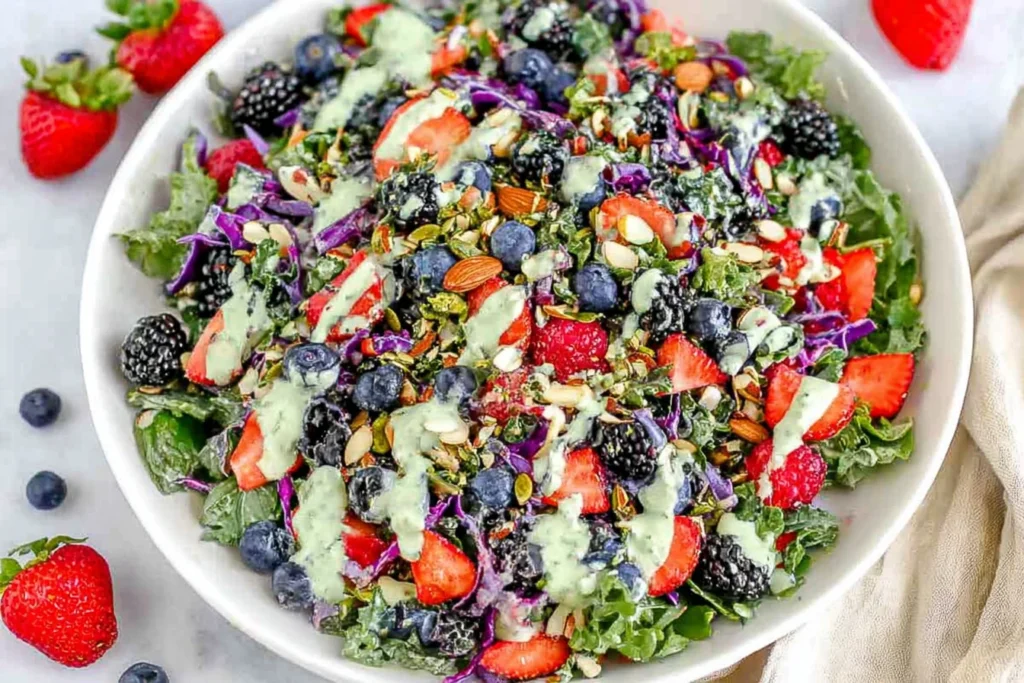 Berry Salad with Creamy Lemon Herb Dressing served in a large white bowl with super greens, kale, strawberries, blueberries, blackberries, and creamy lemon herb drizzle.