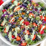 Berry Salad with Creamy Lemon Herb Dressing served in a large white bowl with super greens, kale, strawberries, blueberries, blackberries, and creamy lemon herb drizzle.
