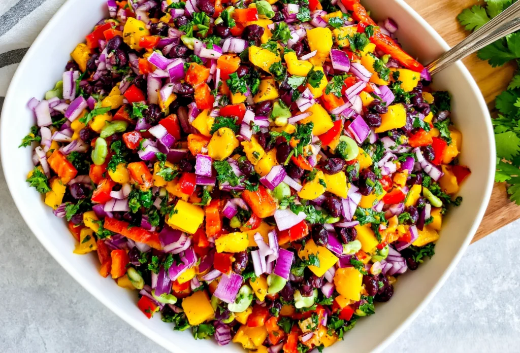 Black Bean Mango Salad with diced mango, black beans, red onion, red bell pepper, cilantro, cucumber, and lime dressing in a white bowl