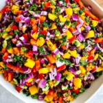 Black Bean Mango Salad with diced mango, black beans, red onion, red bell pepper, cilantro, cucumber, and lime dressing in a white bowl