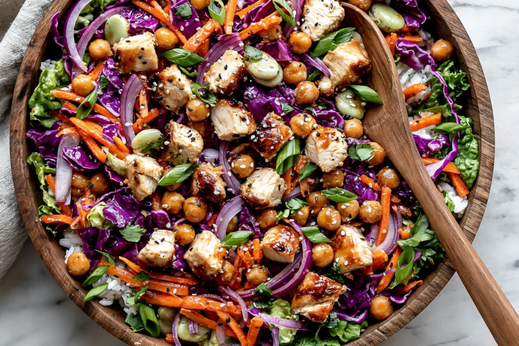 Sesame Chicken and Chickpea Salad in a wooden bowl with chicken, chickpeas, red cabbage, carrots, green onions, sesame seeds, and sesame-ginger dressing