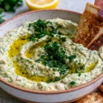 Lemon & Herb White Bean Dip topped with fresh parsley and olive oil, served in a bowl with toasted bread and crackers for a healthy Mediterranean appetizer.
