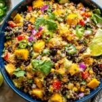 Overhead bowl of Fiesta Mango Quinoa Salad with black beans, corn, red pepper, cilantro, jalapeño, and lime wedges.