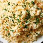 Close-up of fluffy Mediterranean Butter Rice garnished with chopped parsley and a light sprinkle of paprika in a white bowl.