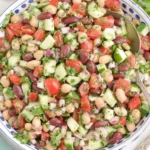 Mediterranean Bean Salad in a white bowl with chickpeas, kidney beans, cucumbers, tomatoes, herbs, and lemon slices.