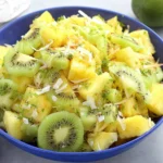 Pineapple Kiwi Salad in a blue bowl with honey-lime dressing, fresh mint, and toasted coconut.