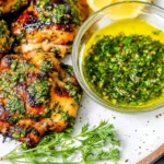 Chimichurri Chicken Thighs grilled until juicy, topped with fresh herb chimichurri, served with a bowl of green sauce and lemon slices.