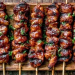 Grilled Thai Coconut Chicken Skewers with sticky coconut glaze, charred edges, and fresh herbs on a wooden platter