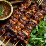Grilled Thai Coconut Chicken Skewers with caramelized coconut glaze, peanut dipping sauce, and fresh cilantro on a serving plate