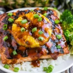 Hawaiian Grilled Salmon topped with grilled pineapple, glossy teriyaki-style glaze, scallions, rice, and broccoli on a white plate