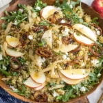 Honey Mustard Quinoa Apple Salad with arugula, crisp apple slices, toasted pepitas, parmesan, and crispy shallots in a wooden bowl.