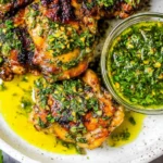 Chimichurri Chicken Thighs on a plate with bright green chimichurri sauce in a jar, grilled and juicy with herbs and garlic.