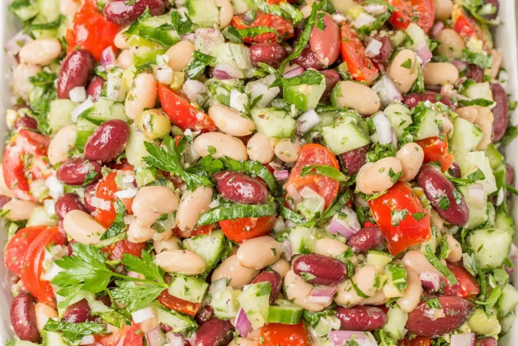 Close-up of Mediterranean Bean Salad with garbanzo beans, cannellini beans, kidney beans, cucumber, tomatoes, herbs, and red onion in lemon dressing.