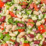 Close-up of Mediterranean Bean Salad with garbanzo beans, cannellini beans, kidney beans, cucumber, tomatoes, herbs, and red onion in lemon dressing.