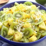 Pineapple Kiwi Salad in a blue bowl with toasted coconut, fresh mint, and honey-lime dressing.