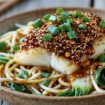Crusted Cod with Aromatic Ginger Noodles topped with sesame seeds, green onions, and bok choy in a cozy bowl