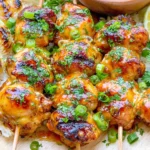 Spicy Honey-Lime Chicken skewers served over fluffy rice with grilled onions, fresh cilantro, green onions, and lime wedges