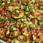 Thai Cucumber Salad with Chicken in a bowl with sliced cucumbers, shredded chicken, green onions, sesame seeds, jalapeños, and chili crisp peanut dressing.