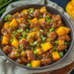 Close-up bowl of Mango Chicken Stir Fry with crispy chicken, sweet-spicy glossy sauce, mango chunks, bell peppers, and green onions.