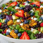 Strawberry Avocado Corn Salad in a large bowl with grilled corn, strawberries, blueberries, avocado, goat cheese, mixed greens, and honey mustard vinaigrette.