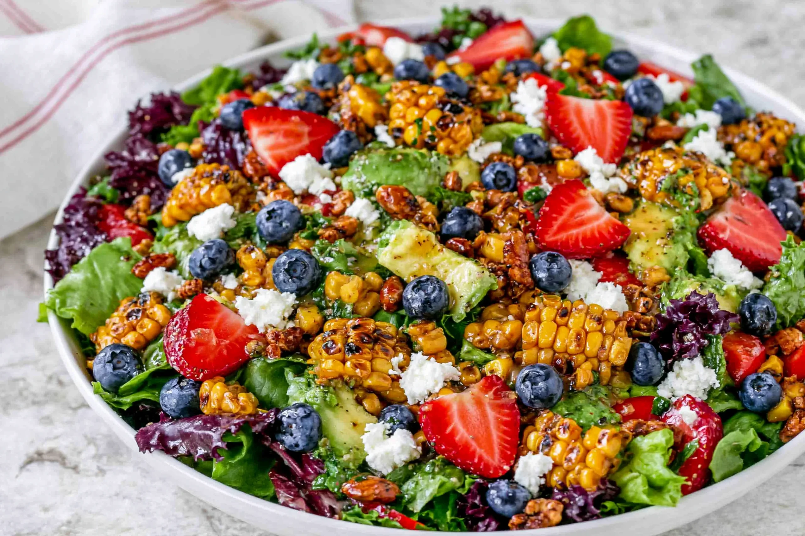 Strawberry Avocado Corn Salad with grilled corn, strawberries, blueberries, goat cheese, and greens, drizzled with honey mustard vinaigrette.