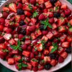 Watermelon Fruit Salad with lime mint dressing, fresh strawberries, raspberries, blackberries, cherries, and mint in a pink serving bowl