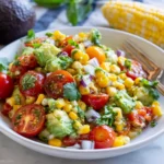 Avocado and Corn Summer Salad with cherry tomatoes, red onion, cilantro, and fresh lime dressing in a white bowl