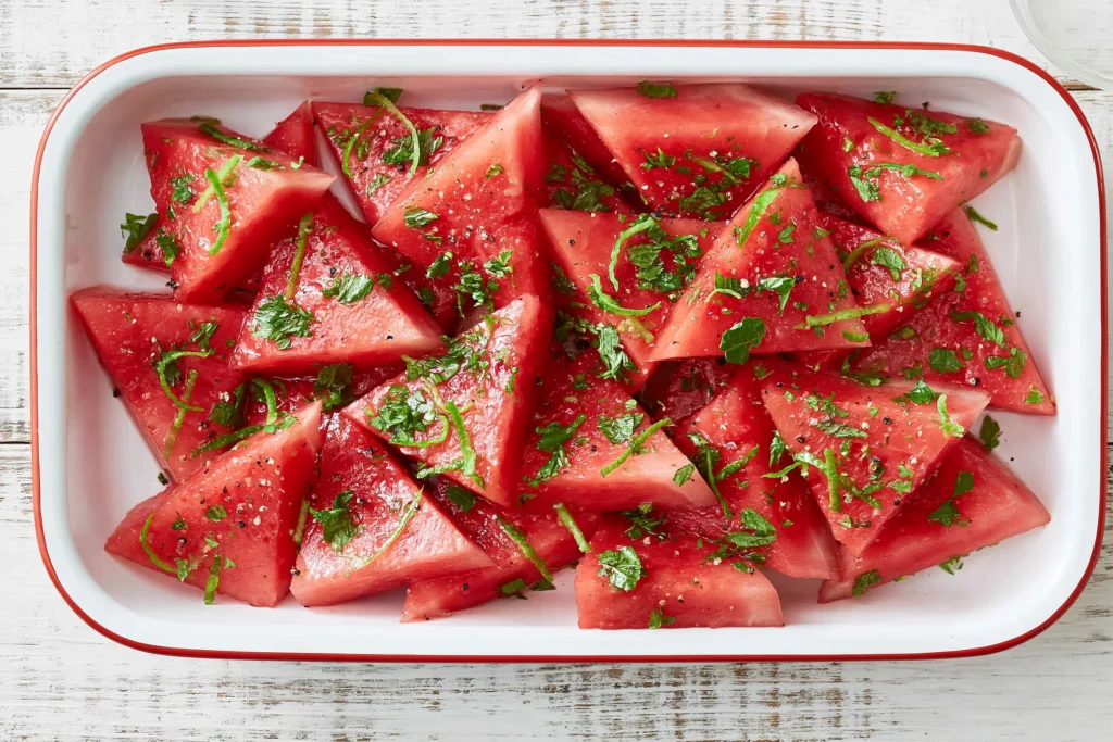 Mojito Watermelon wedges with fresh mint, lime zest, black pepper, and flaky sea salt in a white serving dish