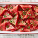 Mojito Watermelon wedges with fresh mint, lime zest, black pepper, and flaky sea salt in a white serving dish